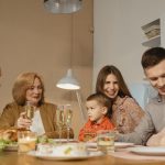 Smiling family of multiple generations enjoying a meal together indoors, sharing laughter and drinks.