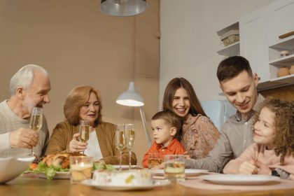Smiling family of multiple generations enjoying a meal together indoors, sharing laughter and drinks.