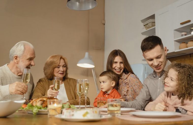 Smiling family of multiple generations enjoying a meal together indoors, sharing laughter and drinks.