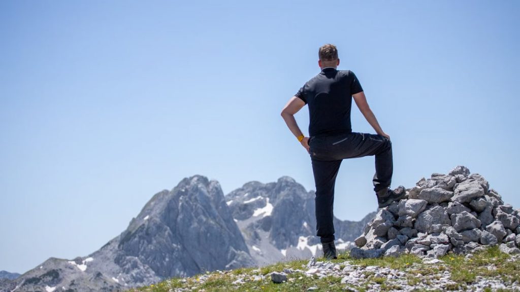 A hiker stands atop a rocky peak, enjoying a breathtaking mountain view on a clear day.