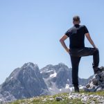A hiker stands atop a rocky peak, enjoying a breathtaking mountain view on a clear day.