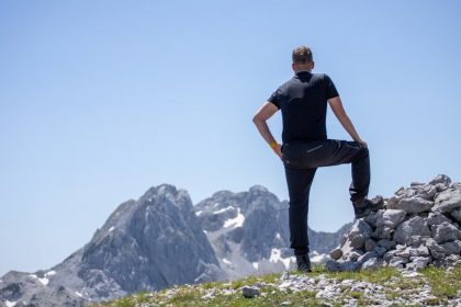 A hiker stands atop a rocky peak, enjoying a breathtaking mountain view on a clear day.