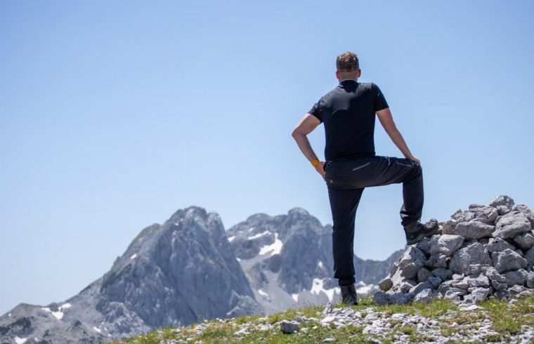 A hiker stands atop a rocky peak, enjoying a breathtaking mountain view on a clear day.